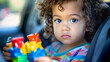 © BetterPhoto - A young child with curly hair holding colorful toys, seated in a car, representing innocence, curiosity, and the joys of childhood.