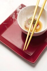 A pair of yellow chopsticks resting on a white bowl, which is placed on a red rectangular plate