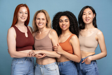 Diverse group for multinational smiling women wearing stylish top and tank top, hugging posing