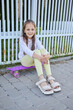 © sementsova321 - Smiling cheerful happy Caucasian little girl skater in casual attire sitting on her her skateboard having fun outdoors in the urban city enjoying active lifestyle and summer holiday