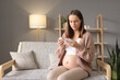© sementsova321 - Serious concentrated young pregnant woman wearing casual clothing using smartphone for checking clinic app illness reading online instruction while sitting on sofa