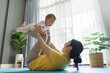 © eggeeggjiew - Asian Mother lifting smiling baby during exercise at home. Indoor lifestyle photography with plants in background. Family and fitness concept
