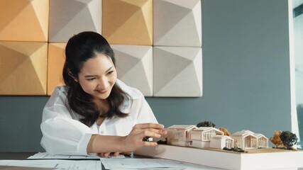 Wall Mural - Portrait of beautiful young architect engineer measures house model while taking a note on blueprint with laptop, project plan and blueprint placed on table. Business design concept. Manipulator.