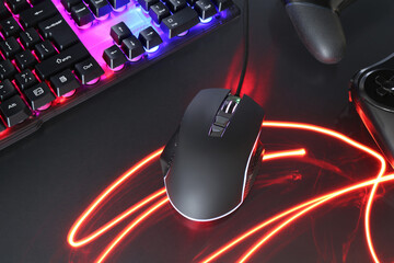 Computer mouse, RGB keyboard and game controllers in neon lights on dark background, closeup