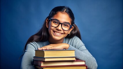 Vibrant smiling Hispanic teenage girl with glasses sits amidst stacked books on a dark blue background with ample copy space.