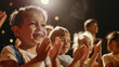 © VK Studio - Enthusiastic children in an audience cheerfully applauding, their faces vividly glowing under a spotlight.