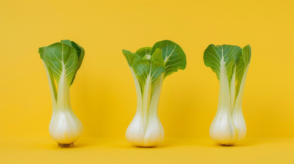 Wall Mural - Three stalks of vibrant bok choy are neatly displayed against a bold yellow background, creating a playful and fresh visual contrast.