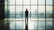 © VK Studio - A silhouette of a person stands alone in a modern glass-walled building, gazing at the sprawling cityscape outside.