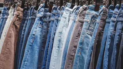 Poster - A row of jeans hanging on a rack. The jeans are of different colors and styles. Concept of variety and choice, as the person hanging the jeans can pick from a wide range of options