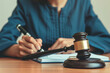 © tonstock - Female judge writing verdict in courtroom. Legal gavel on wooden table. Justice and law concept. Professional judiciary scene.