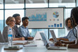 © tynza - A diverse group of business professionals in a modern office, gathered around a conference table, discussing and collaborating with laptops, charts, and graphs in front of them.