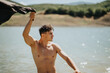 © qunica.com - Young shirtless man enjoying a sunny day by the lake. The man throws a towel over his shoulder, feeling the breeze.