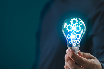 hand holding light bulb with glowing gears symbolizing ideas, innovation, and technology. blue backg