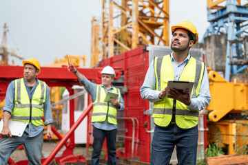 asian male engineer wearing safety vests and helmet with tablet look at tower crane for maintenance.