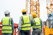 © Supachai - Group of male engineer wearing safety vests and helmet pointing to tower crane for surveying and maintenance at construction site.