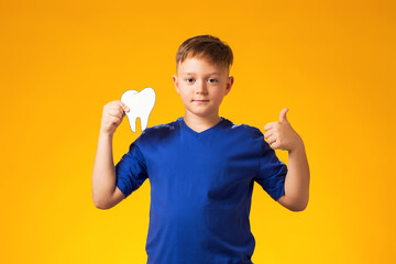 Child boy holding papercraft tooth and showing thumb up gesture. Dental health concept