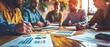 © Inlovehem - Team brainstorming session with business professionals discussing graphs and charts at a wooden table in a modern office setting.