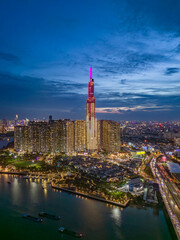 Wall Mural - Landmark building illuminated night drone shot with Saigon river boat traffic and road traffic on the bridge below in vertical format. A dramatic welcome to Ho Chi Minh City, Vietnam.