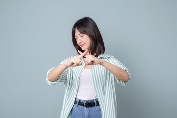 Wall Mural - serious asian woman shows cross hands gesture, stop sign, taboo, disapproves bad action, stands in white and green shirt over pastel green background