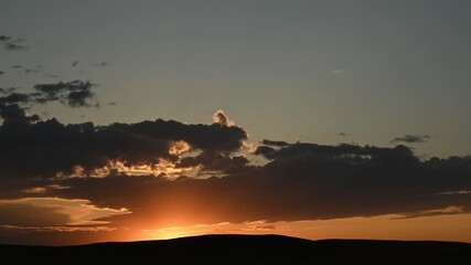 Wall Mural - time lapse of late evening clouds reflect the sun as it sets behind low rolling hills. the sunset in
