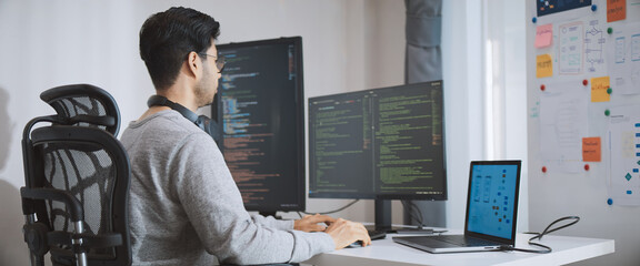 Young adult Asian male software developer coding program on desktop computer. Man work from home, remote working, freelance programmer job, smart digital nomad lifestyle concept