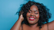 © Ron - beautiful smiling black woman plus size model with red lipstick and curly hair, posing for photo shoot, blue background for lipstick or hair brand campaign
