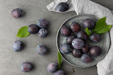 Wall Mural - Retro plate with whole fresh ripe plum fruits and leaves on dark grey stone table background.