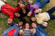 © Aida - Diverse happy teenagers lying in a circle on the grass putting their hands together