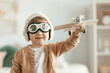 © forenna - Joyful toddler boy dressed as an aviator pilot, wearing goggles and holding a toy airplane in his room. Child's imagination, dream, playful freedom, creative playtime photo