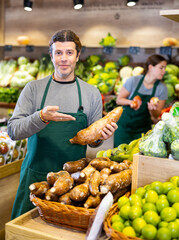 Wall Mural - Adult man in apron sells cassava in vegetable shop