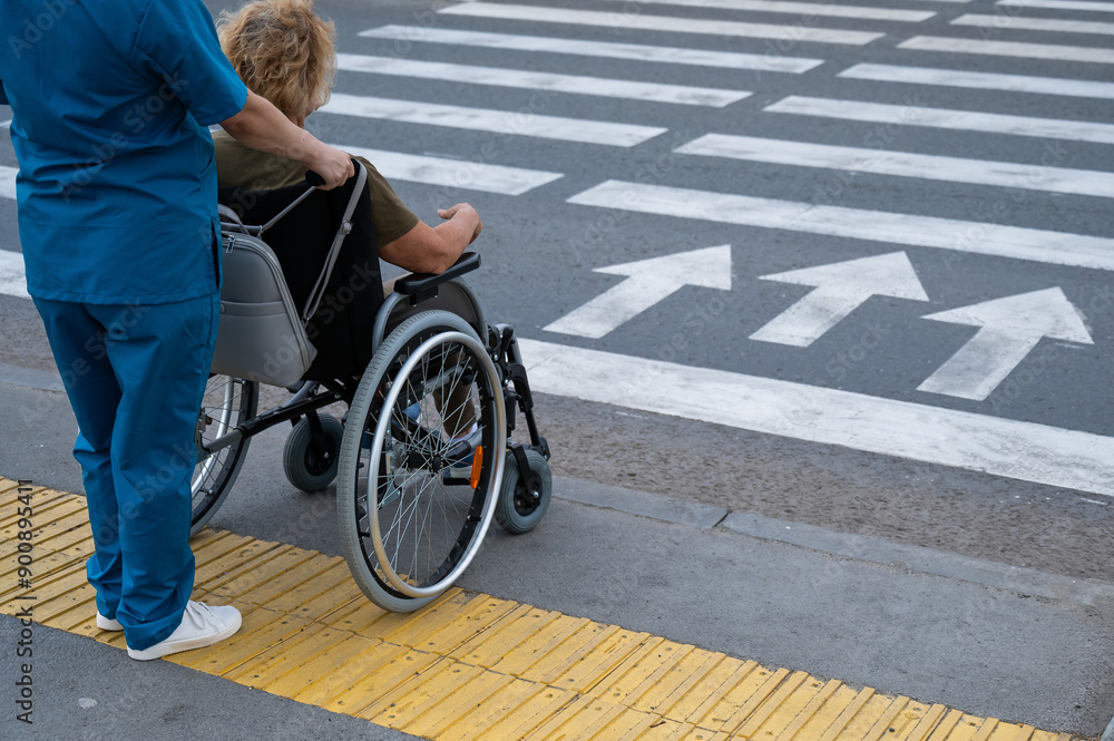 Rear view of a nurse helping an elderly woman in a wheelchair cross the ...