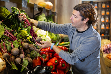 Wall Mural - Satisfied man chooses beets in the vegetable section of the supermarket