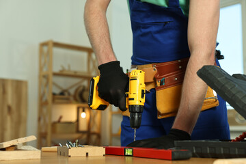 Wall Mural - Craftsman working with drill at wooden table in workshop, closeup. Space for text