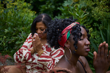 Portrait of two women meditating in a park surrounded by lush greenery.