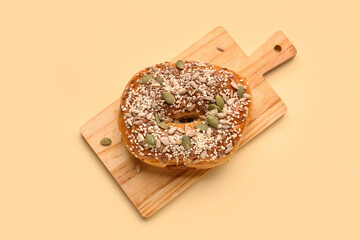 Wall Mural - Wooden board of tasty bagel with sesame and pumpkin seeds on beige background