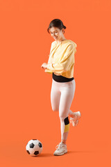 Wall Mural - Young woman in sportswear playing with soccer ball on orange background