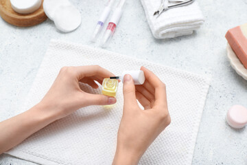 Female hands with bottle of cuticle oil and towel on light background