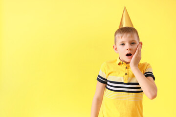 Wall Mural - Shocked little boy in party cone on yellow background