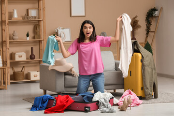 Wall Mural - Surprised woman with clothes and suitcases near grey sofa in living room