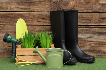 Wall Mural - Composition with watering can, rubber boots and water sprayer on green grass against wooden background