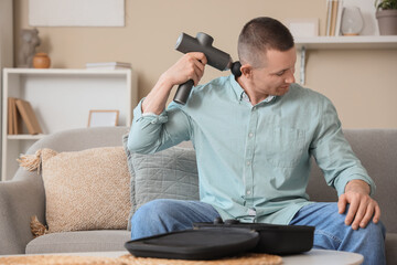 Sticker - Young man massaging his neck with percussive massager at home