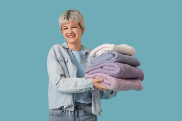 Poster - Beautiful young woman holding stack of clean clothes on blue background