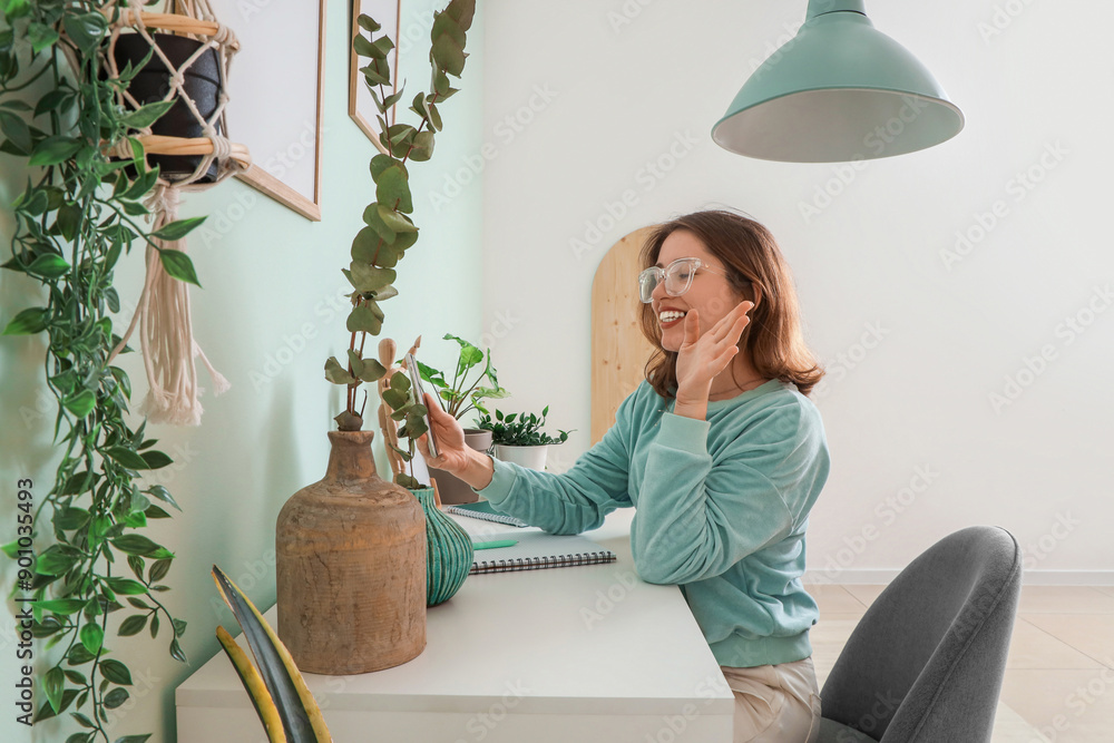 Young woman using mobile phone at desk with eucalyptus branches in office