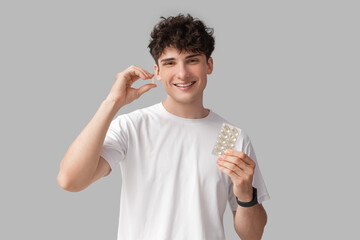 Wall Mural - Young man with fish oil on grey background