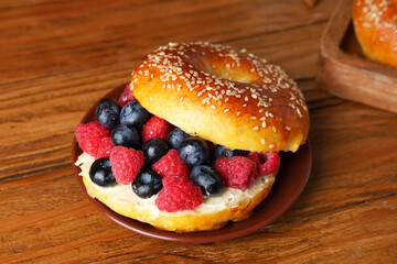 Wall Mural - Plate of tasty bagel with butter and berries on wooden background