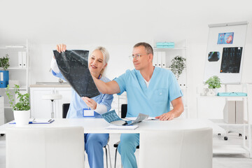 Wall Mural - Mature doctors studying x-ray image of spine at table in clinic