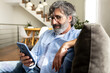 © Daniel - Mature man relaxing at home, sitting on the sofa sending text message with mobile phone.
