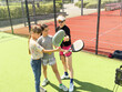 © Angelov - Cheerful coach teaching child to play padel tennis while both standing on tennis court