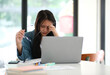 © ijeab - A woman is sitting at a table with a laptop and a stack of papers