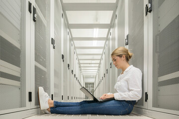 Woman engineer sitting and working on laptop in data server room